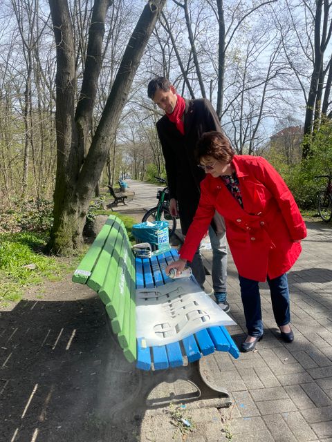 Bezirksbürgermeister Hikel lackiert mit Spenderin Gabriela Gebhard die zweite Sitzbank im Park am Buschkrug