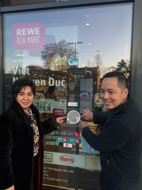 Eine weitere Anlaufstelle: Bezirksbürgermeisterin Emine Demirbüken-Wegner und Geschäftsführer des REWE Markts in Tegel Herr Duc Viet Nguyen zeigen auf den Sticker gegen Einsamkeit