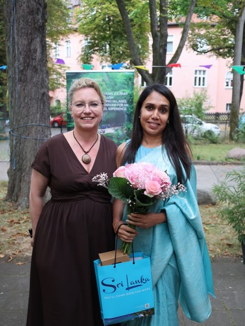 7. Juli 2026: Thivanka Athuraliya, Chargé d'affaires der srilankischen Botschaft (rechts im Bild), nimmt Blumen von Stefanie Müller, Leiterin des Kommunikationszentrums am Ostpreußendamm, entgegen