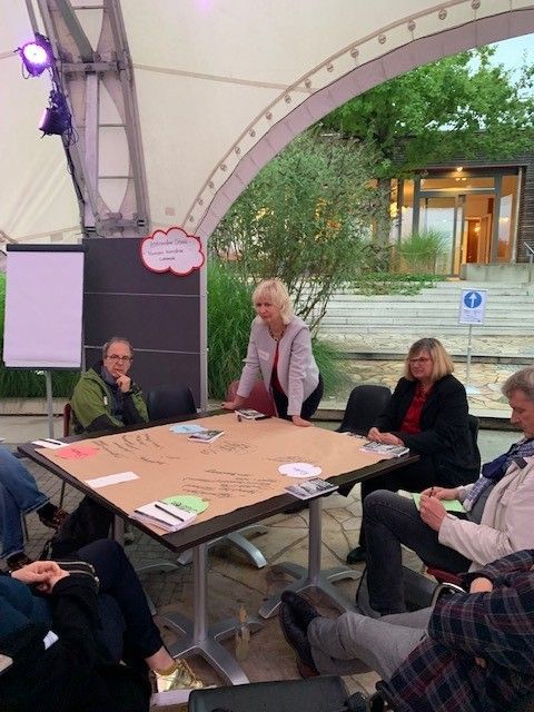 Mehrere Menschen sitzen in einem Stuhlkreis um einen Tisch und reden miteinander.