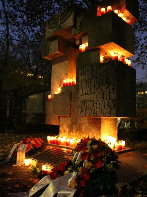 Ein Denkmal mit vielen Kerzen und Sträußen in der Dämmerung.