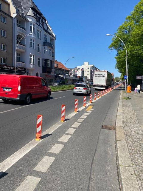 Auf einer Straße ist ein Fahrradstreifen mit Pollern und Fahrbahnmarkierungen abgetrennt.