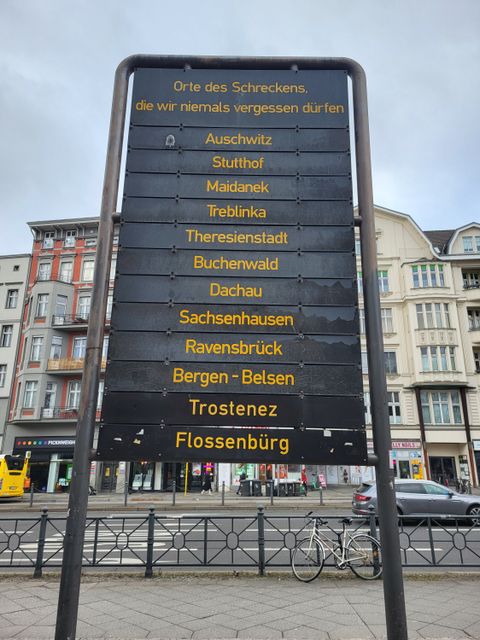 Eine schwarze Tafel mit der Überschrift "Orte des Schreckens, die wir niemals vergessen dürfen" und der Auflistung folgender Orte: Auschwitz, Stutthof, Maidanek, Treblinka, Theresienstadt, Buchenwald, Dachau, Sachsenhausen, Ravensbrück, Bergen-Belsen, Trostenez, Flossenbürg