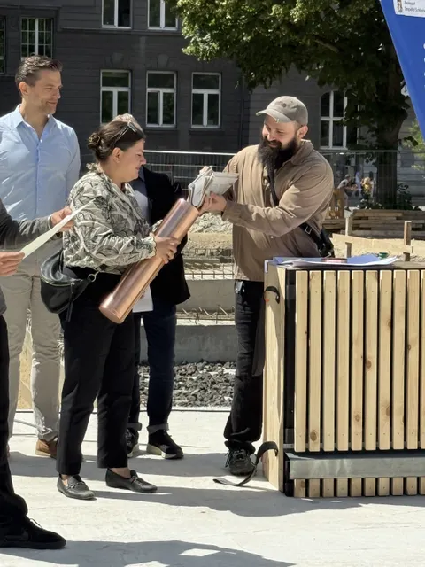 Frau hält ein Rohr in der Hand, das mit Zeitungen befüllt wird.