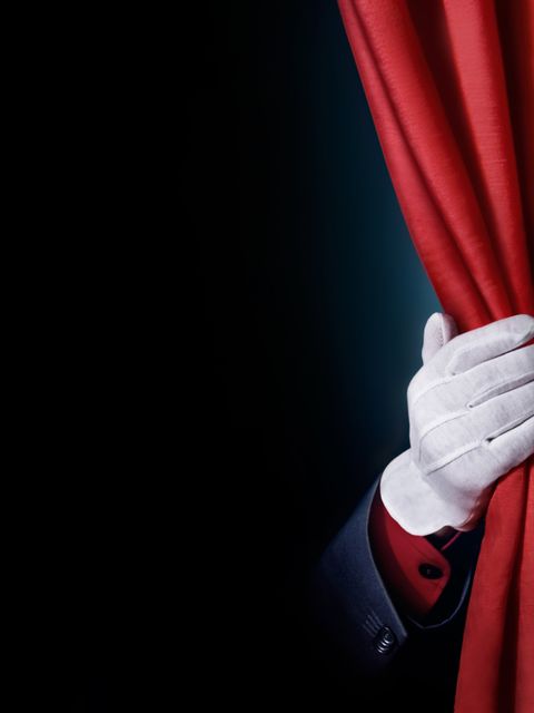 Das Bild zeigt einen Bühnenvorhang der von einer Hand beiseite geschoben wird