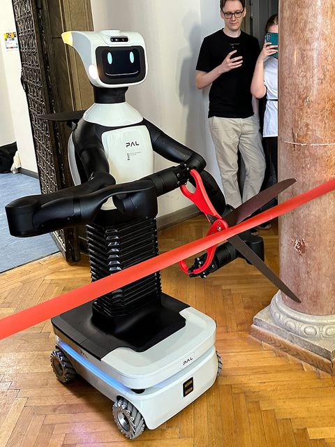 Ein Roboter auf Rollen mit einem lächelnden Gesicht zerschneidet ein rotes Band