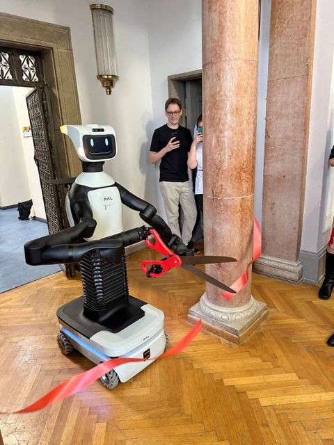 Ein Roboter auf Rollen zerschneidet mit einer roten Schere ein rotes Band