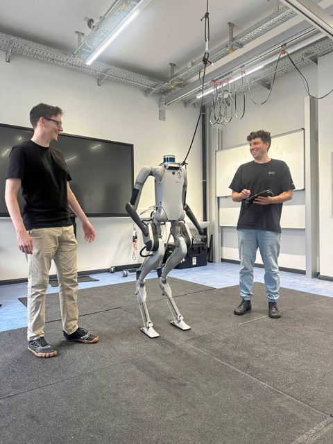Zwei junge Männer stehen neben einem zweibeinigen Roboter