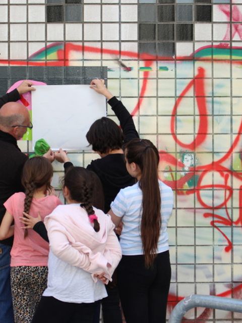 Workshopleiter und Schulkinder bekleben die Wand mit bunter Folie.