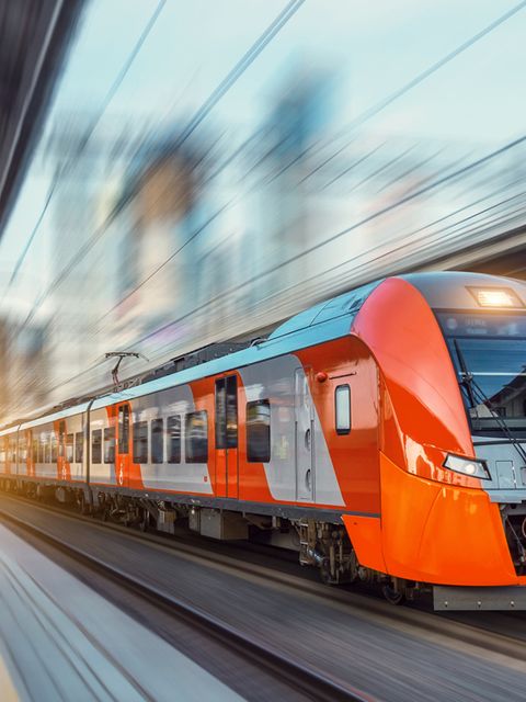 Electric passenger train drives at high speed among urban landscape.