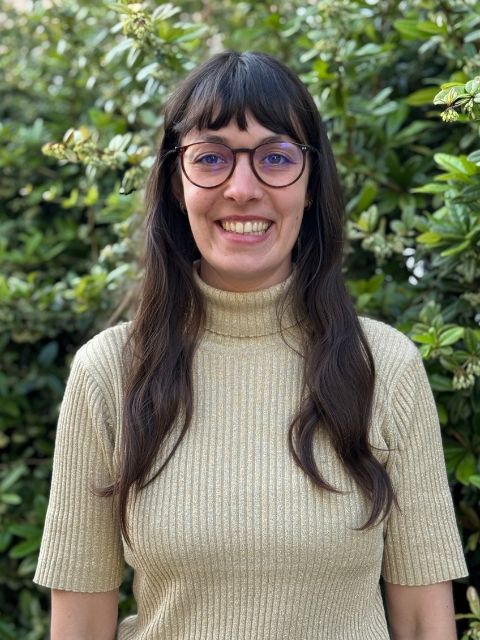 Kursleiterin Sophia Hörhold steht vor einer grünen Hecke und lächelt in die Kamera.