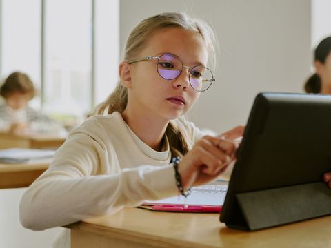 Schülerin sitzt im Klassenzimmer und benutzt ein Tablet