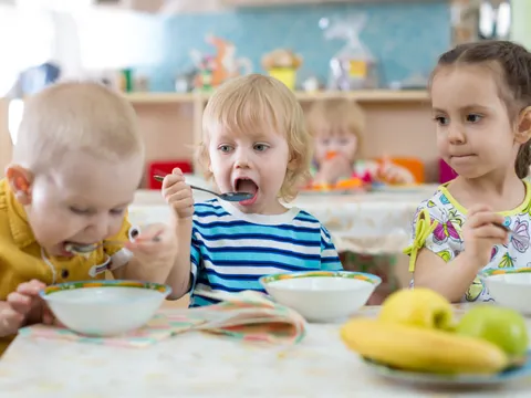 Gruppe von Kindern isst im Kindergarten von Tellern
