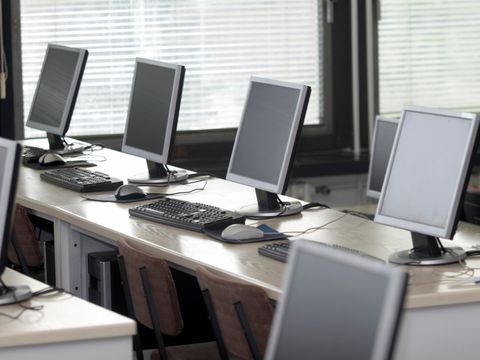Reihe von Computermonitoren, Tastaturen und Mäusen auf einem langen Tisch in einem Computerraum