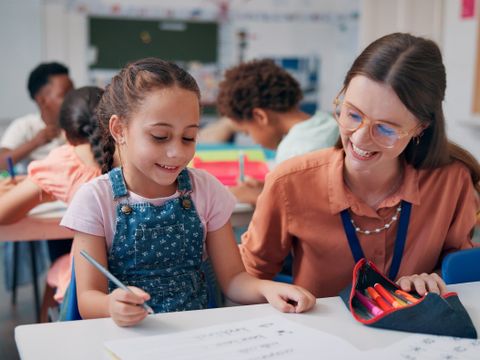 Mädchen und Lehrkraft im Klassenzimmer am Tisch, unterstützendes Lernen