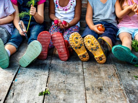 Sitzende Kinder mit Gummistiefeln halten Gemüse in den Händen