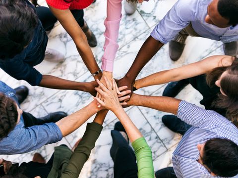 Gruppe von Menschen, die im Kreis stehen und ihre Hände in der Mitte übereinanderlegen