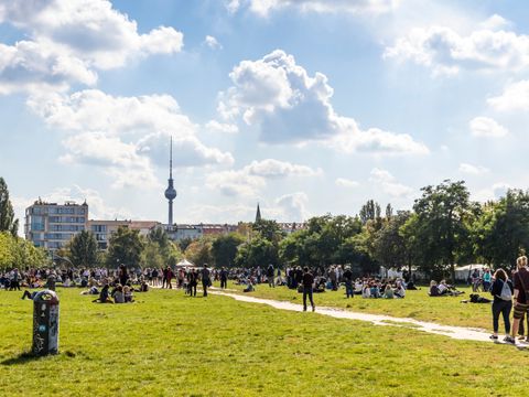 Berliner Mauerpark mit vielen Menschen, die in Gruppen sitzen oder stehen, im Hintergrund der Fernsehturm und Gebäude
