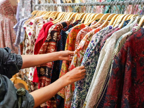 Nahaufnahme der Hand einer Frau, die im Geschäft ein farbenfrohes T-Shirt mit Rabatt auswählt; Suche nach oder Kauf eines günstigen Baumwollshirts auf einem Kleiderständer – Konzept für Modeeinkauf und Marktbummel.