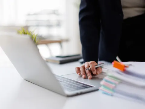 Frau arbeitet an einem Laptop und Papierstapel