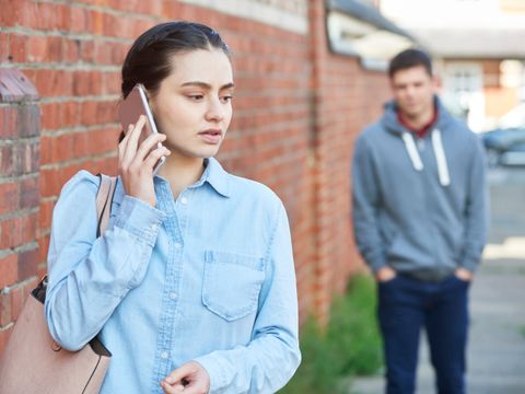Häusliche Gewalt - eine Frau ruft mit dem Handy nach Hilfe, weil sie von einem Mann gestalkt wird