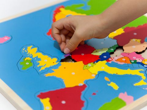 Hand eines Kindes, das ein Puzzleteil in eine bunte Europakarte aus Holz einfügt