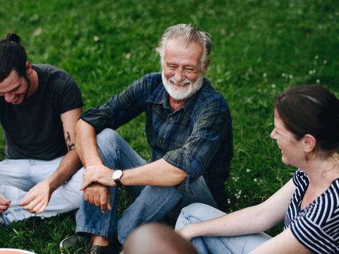 Drei Personen sitzen im Gras und unterhalten sich entspannt in lockerer Kleidung