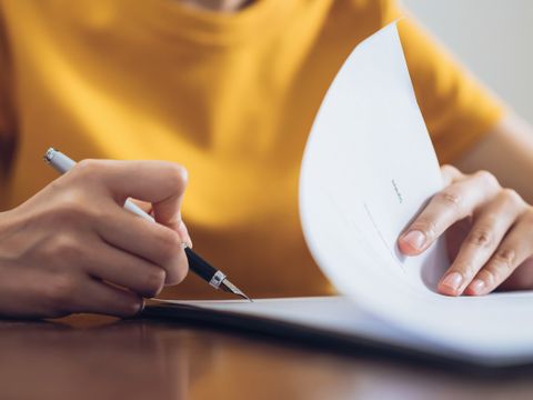 Eine Frau unterzeichnet ein Dokument und hält dabei den Stift in der Hand