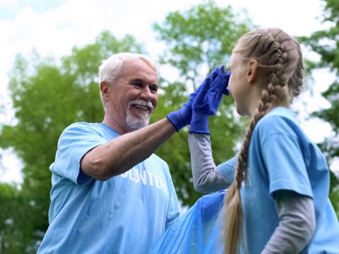 Älterer Mann und junges Mädchen mit blauen T-Shirts und Handschuhen geben sich im Freien einen High-Five