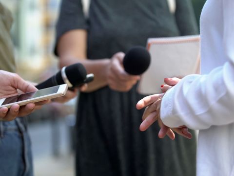 Zwei Personen mit Mikrofonen und Smartphones, die eine dritte Person interviewen