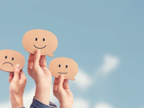 Hände zeigen Bewertungen mit Smileys vor Himmelshintergrund