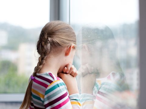 Sad child looking through rainy window at home. Upset kid in self isolation during quarantine.