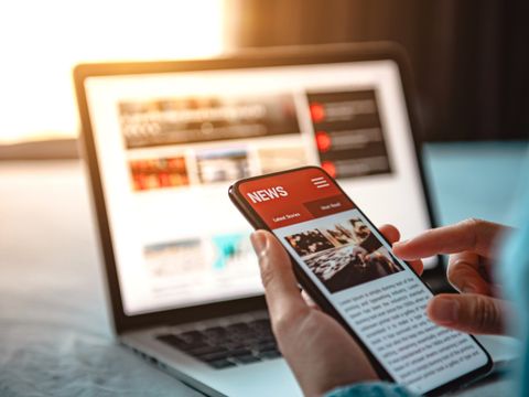 Online news on a smartphone. Mockup website. Woman reading news or articles in a mobile phone screen application at home. Newspaper and portal on internet.