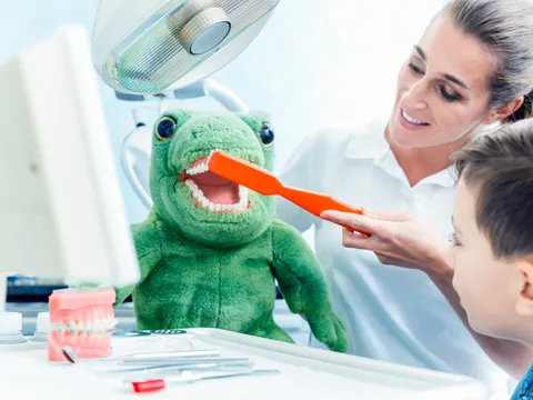 Boy looking at doctor brushing the dinosaur's teeth in clinic