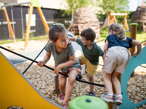 Drei Kinder spielen auf einem Klettergerüst im Freien mit Holzschnitzelboden