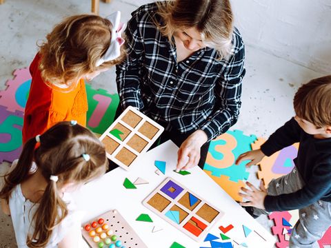Erzieherin und Kinder puzzeln gemeinsam