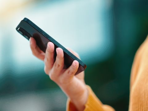 Hand hält ein schwarzes Smartphone vor unscharfem Hintergrund