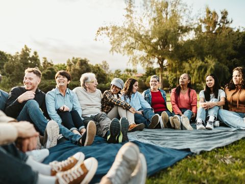 Gruppe verschiedener Menschen sitzt auf einer Decke im Freien und lacht