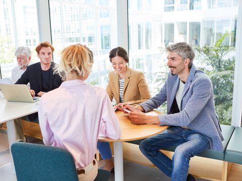 Eine fröhliche Gruppe von Geschäftsleuten, die gemeinsam am Tisch in der Büropause sitzen und sich unterhalten