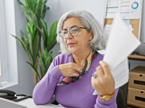 eine Frau in einem Büro fächert sich mit einem Blatt Papier Luft zu, um die Hitze am Arbeitsplatz auszuhalten.