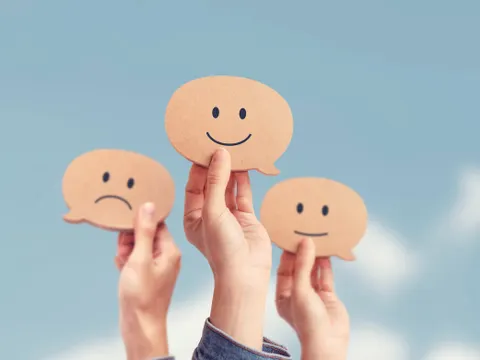 Hände zeigen Bewertungen mit Smileys vor Himmelshintergrund