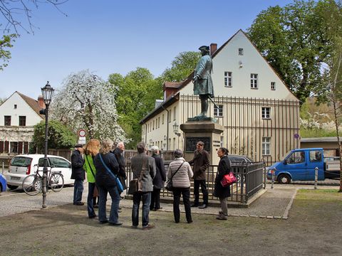 Eine Führung durch das Böhmische Dorf in Neukölln; im Hintergrund das Denkmal von Friedrich-Wilhelm I., das 1912 aus Dankbarkeit von Nachfahren der Emigranten errichtet wurde