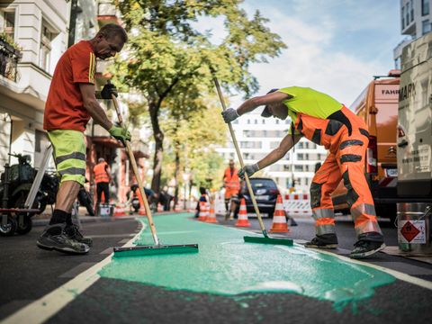 Zwei Menschen Arbeitskleidung tragen eine grüne Beschichtung auf einem Radweg auf.