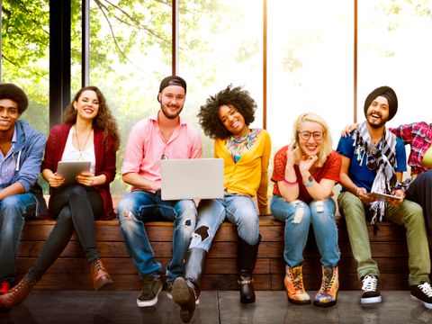 Junge Menschen diverse Herkunft sitzen lächelnd auf einer Bank
