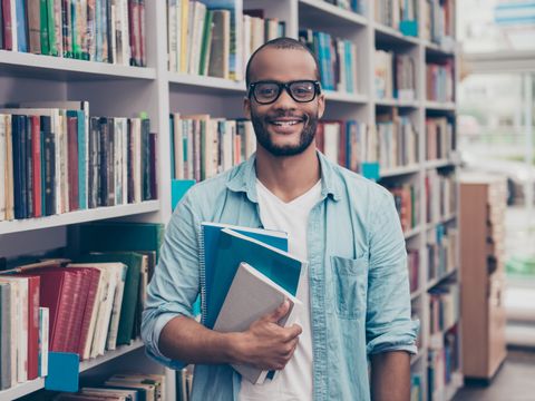 Junger Student aus Afrika mit Büchern in der Hand in einer Bibliothek