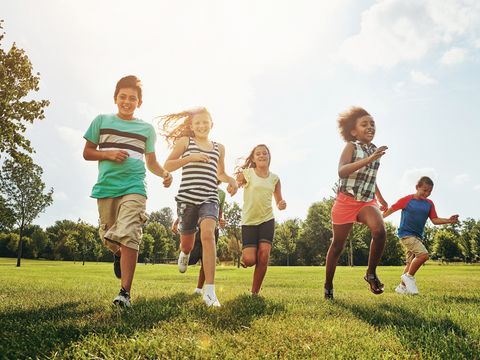 Happy friends, children and running with grass field in nature for fun, playful day or sunshine at park. Diversity or group of excited kids or youth enjoying sunny outdoor holiday or weekend together