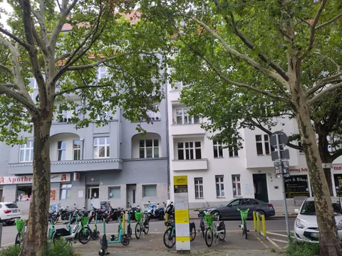 gelbe Info-Stele und viele leihbare Räder und Roller zwischen 2 Bäumen am Fahrbahnrand