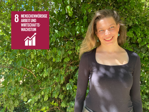 Helena Jansen lächelnd vor einer grün bewachsenen Wand mit SDG-8 Logo