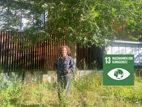 Annie Stamm-Grossjohann steht im Garten der Pablo-Neruda Bibliothek vor einem Baum. Digital eingefügt ist eine grüne Kachel mit dem Nachhaltigkeitsziel 13: Maßnahmen zum Klimaschutz