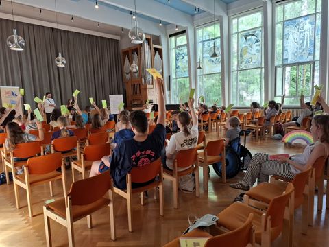 Kinder und Jugendliche sitzen in großem Saal